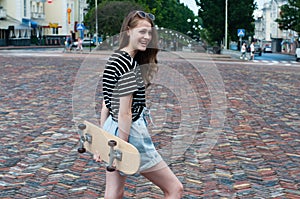 Pretty teenager girl with a skateboard in the center of a European city