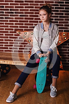 Pretty teenager girl with skateboard sitting in studio