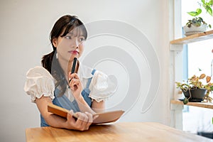 A pretty and thoughtful young Asian woman is thinking creative ideas, keeping her diary at a cafe