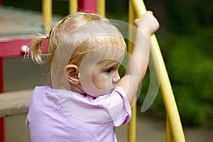 Pretty toddler girl with cute little pony tail on the playground on a beautiful summer day