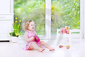 Pretty toddler girl playing tambourine in white room