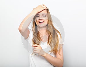 Pretty toothy laughing young woman with fair blond long hair in casual dress holding the head the hands. Studio shot of good