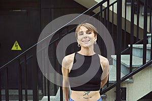 Pretty townswoman with tattoo on her stomach is standing at stairs photo