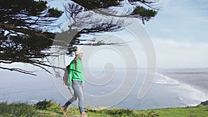 Pretty traveler woman in beanie hat walking edge of hill with scenic landscape