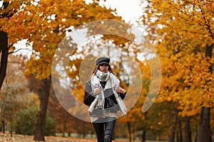 Pretty trendy young woman in a fashion hat with a bag in a vintage jacket in leather leggings with a scarf travels through the