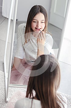 Pretty tween girl rouge lips holding red lipstick looking at big mirror