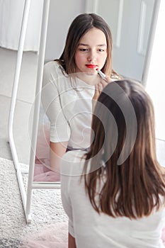 Pretty tween girl rouge lips holding red lipstick looking at big mirror