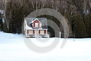 Pretty view of a cute small dark red traditional French-style cottage with sloped shingled roof seen in winter