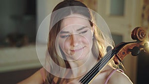 Pretty violoncellist sitting on bed and playing the melody in bedroom