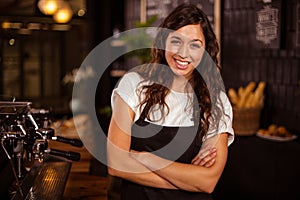 Pretty waitress posing with arms crossed next to coffee machine