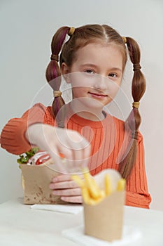 Pretty white girl eats fries and souvlaki in Greek restaurant. Beautiful elementary age kid eating fast food and looking in camera