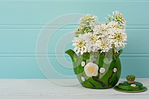 Pretty White Spring Flowers in a Vintage Asian Pot on Wood Table with Teal Boards Background in shabby chic style.  It`s a Horizo