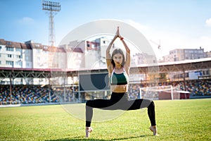 Pretty  woman athlete stretching her body at stadium grass