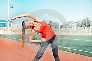 A pretty woman athlete stretching her body at stadium track