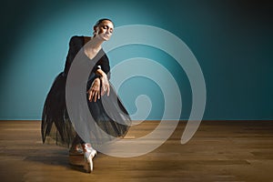 Pretty woman ballerina in tutu and pointe in black swimsuit posing in studio on blue background