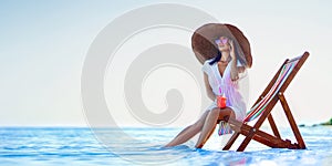 Pretty woman in big straw hat relaxing on a lounger beach and drinks refreshing juice. summer vacation concept