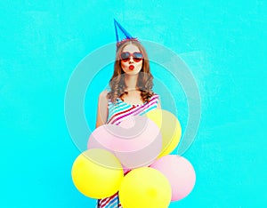 Pretty woman in a birthday cap is sends an air kiss holds an air colorful balloons