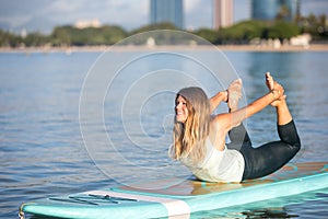 Pretty woman in bow pose doing SUP Yoga on the water photo