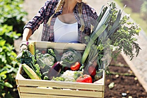 Pretty woman with box of vegetables in her garden