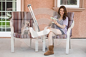 Pretty woman with broken leg in cast relaxing on chair at home with her dog while counting money
