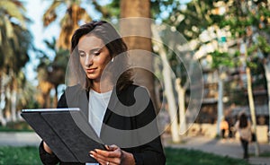 Pretty woman in business suit and wireless earphones selects music using laptop computer while relaxing Park in Barcelona