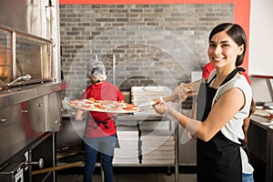 Pretty woman chef putting fresh made pizza in oven