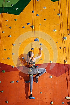 Pretty woman climbing up the orange wall in gym