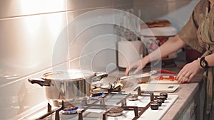 Pretty woman cooking soup on stove at kitchen. Close up of housewife preparing dinner at home. Young woman tasting soup