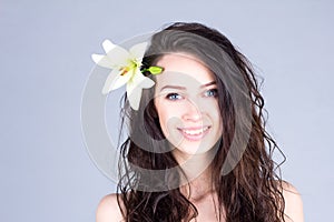 Pretty woman with curly brown hair and a flower in her hair smiling with teeth