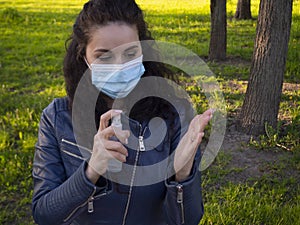 Pretty woman with curly hair in protective medical face mask disinfecting her hands with a sanitizer spray