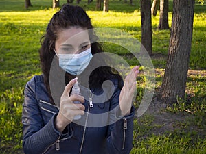 Pretty woman with curly hair in protective medical face mask disinfecting her hands with a sanitizer spray