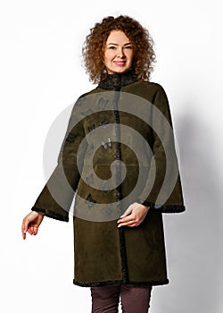 Pretty woman with curly red hair poses in brown sheepskin coat with karakul collar and cuffs and with butterfly embossed