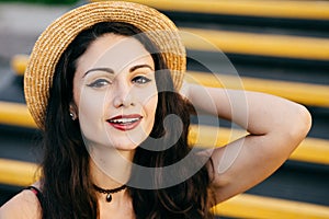 Pretty woman with dark hair, shining eyes and red painted lips looking confidently and with smile at camera wearing straw hat and