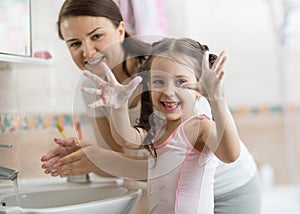 Pretty woman and daughter child girl washing hands with soap in bathroom