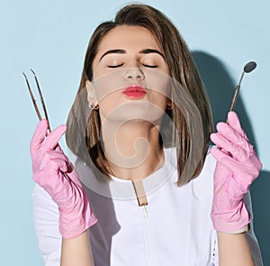 Pretty woman dentist in gloves and uniform holds dental tools and mirror for teeth examination and sends a kiss