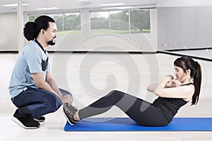 Pretty woman doing sit up with her trainer