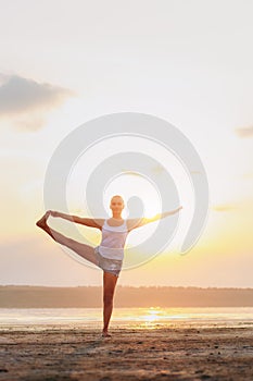 Pretty woman doing yoga at sunset outdoors