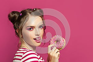 Pretty woman with donut and tongue lick one`s lips on colorful pink background