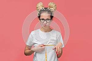 Girl with dreads in a white shirt and glasses looking is upset measuring her boobs photo