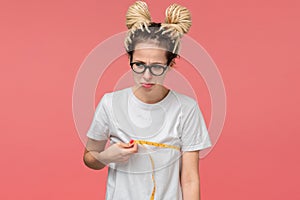 Girl with dreads in a white shirt and glasses looking is upset measuring her boobs