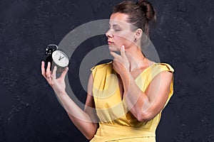 Pretty woman in dress looks at alarm clock