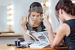 Pretty woman drinking champagne and reading magazine in dressing room