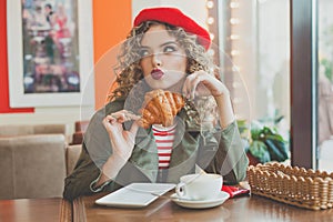 Pretty woman drinking coffee and eating french croissant in european city street cafe