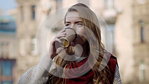 Pretty woman drinking coffee outdoors. Hipster girl enjoying hot drink on city