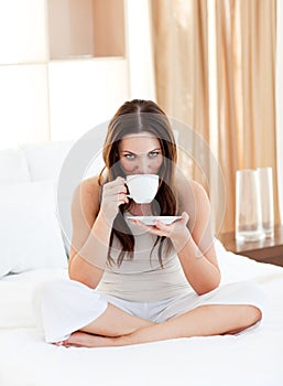 Pretty woman drinking coffee sitting on bed