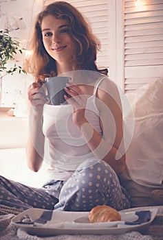 Pretty woman drinking coffee sitting on bed at home
