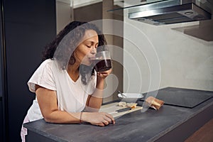 Pretty woman drinking coffee, standing at kitchen counter at home interior. Young happy woman drinks coffee on the