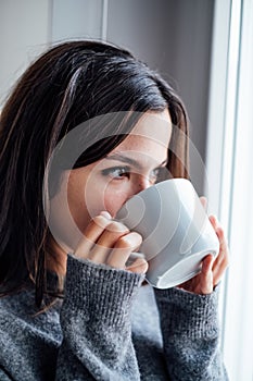 Pretty woman drinking coffee from a white cup and looking out the window