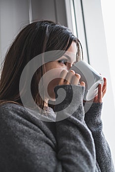 Pretty woman drinking coffee from a white cup and looking out the window