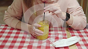 Pretty woman drinks warming sea buckthorn vitamin tea through a straw of glass mug sitting in a cafe in the evening.